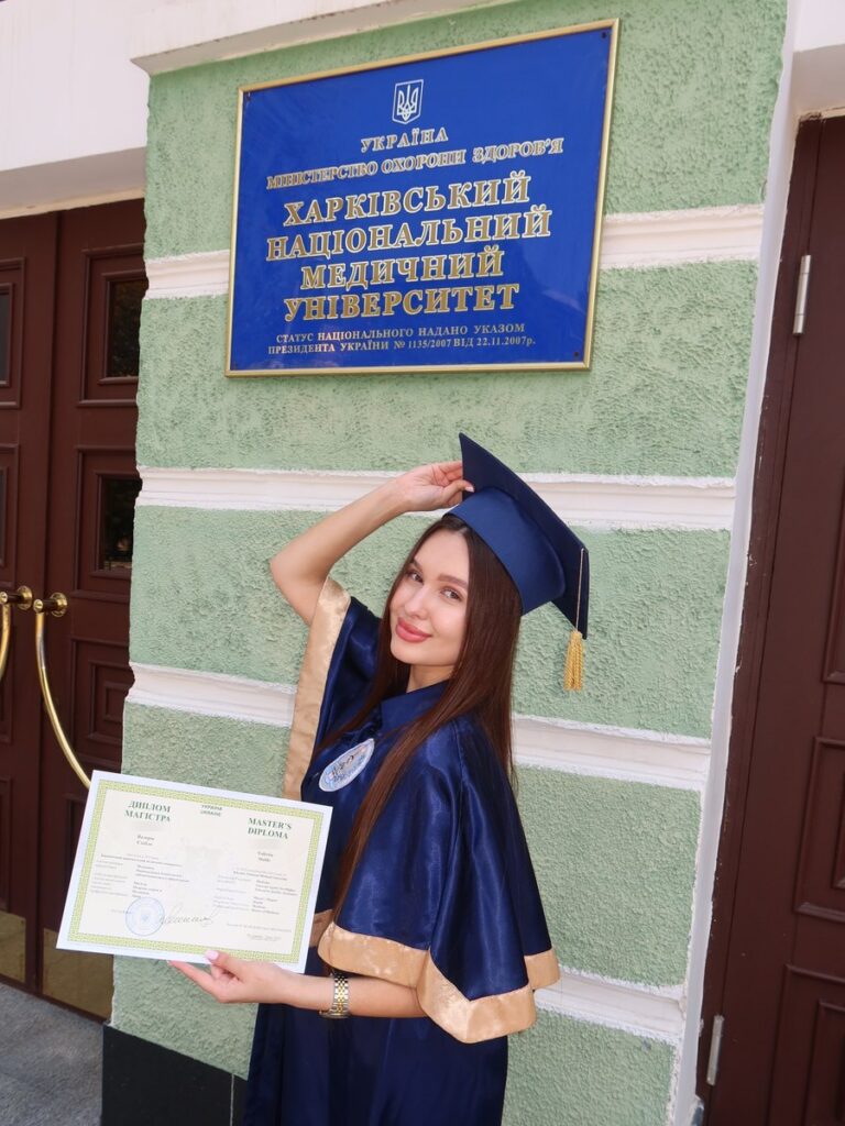 Валерія в мантії з дипломом магістра біля входу до Харківського національного медичного університету